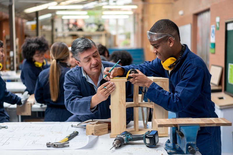 An instructor guiding a young person building a wood frame structure in a workshop